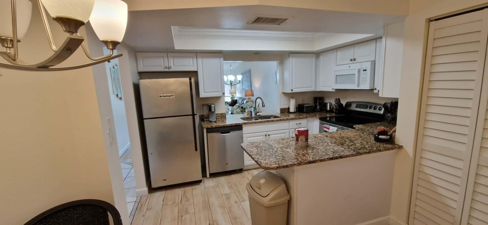A compact kitchen with white cabinets, a stainless steel refrigerator, a dishwasher, and a granite countertop.
