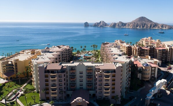 A coastal hotel with multiple buildings, a swimming pool, and a view of the sea and mountains. - IDEAL Location on Medano Beach, fantastic view! Walking distance to everything, swim-up bar, acce... (Cabo San Lucas)