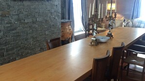 Ein langer Holzesstisch mit Stühlen, ein Pfauengemälde an der Wand und eine rustikale Ziegelwand.