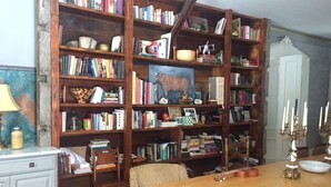 Ein Zimmer mit einer Holzbücherreolen, voll mit Büchern und Dekorationsgegenständen, einem Holzessttisch mit einer Gitarre und einer weißen Tür im Hintergrund.