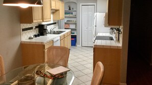 A compact kitchen with wooden cabinets, a white refrigerator, and a dining table with chairs.