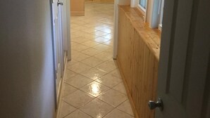 A hallway with tiled flooring, wooden paneling, and a door leading to another room.
