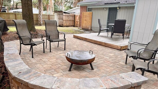 A patio with a stone fire pit, surrounded by chairs and a table.