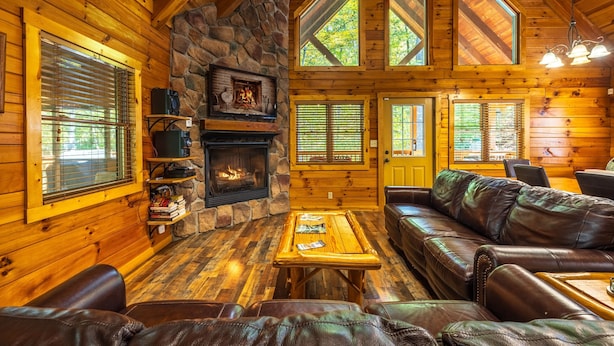 A log cabin interior with a stone fireplace, leather furniture, and large windows. - Cardinal Cabin (Hocking Hills area) (Sugar Grove)