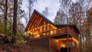 A log cabin with a balcony and string lights, surrounded by trees. - Cardinal Cabin (Hocking Hills area) (Sugar Grove)