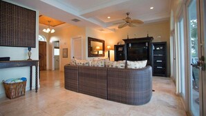 A spacious living room with a large, curved wicker sofa, a ceiling fan, and a large mirror above a fireplace. - 3 Bedroom 3.5 Bath Villa on the Water (Exuma)