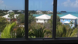 A view of a coastal area with several buildings, including a prominent white building with a blue roof, surrounded by lush greenery and a clear blue sea. - 3 Bedroom 3.5 Bath Villa on the Water (Exuma)