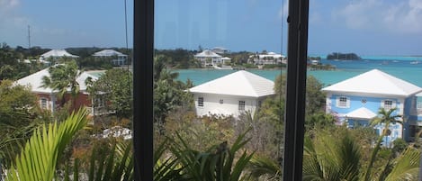 Une vue d’une zone côtière avec plusieurs bâtiments, dont un imposant bâtiment blanc surmonté d’un toit bleu, le tout entouré d’une végétation luxuriante et d’une mer d’un bleu limpide.