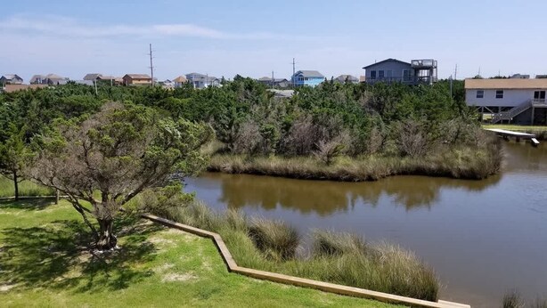 Un lago tranquilo con un muelle de madera, rodeado de abundante vegetación y edificios residenciales al fondo.