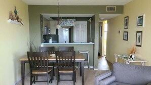 Una sala de estar con un sofá gris, una mesa de comedor con sillas, una cocina al fondo y un pasillo que lleva a otra habitación.