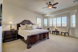 A bedroom with a large bed, two bedside tables, a chair, and a ceiling fan.