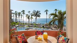 A balcony with a table set for breakfast, overlooking a pool and palm trees. - Beachfront Luxury 3BR Ocean Front Villa – Steps from Pool and Beach! (Cabo San Lucas)