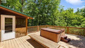 A wooden deck with a hot tub, wooden benches, and a view of a forest.