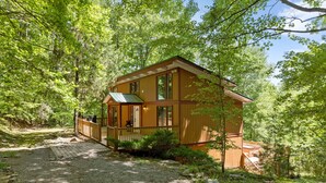 A wooden cabin with a porch, surrounded by dense forest.