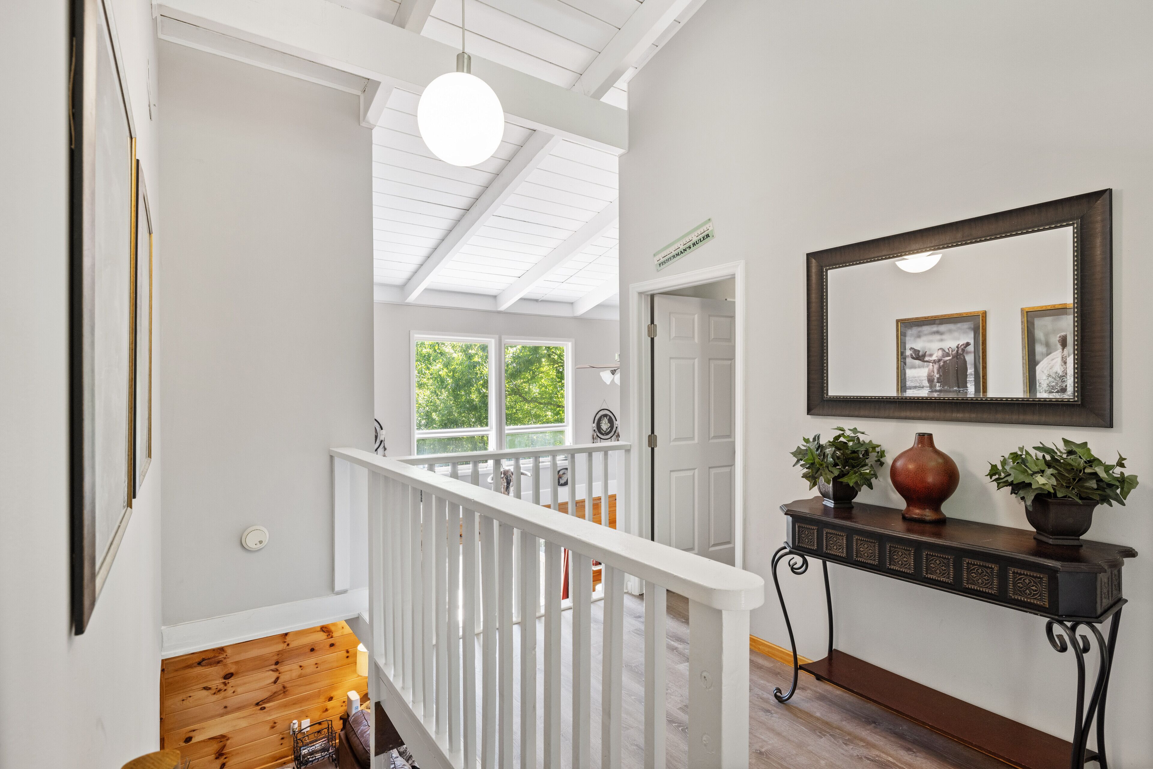 A staircase with white railings leading to a second floor, a console table with two potted plants, and a framed mirror on the wall.