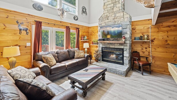A cozy log cabin interior with a stone fireplace, leather sofas, and a mounted animal head.