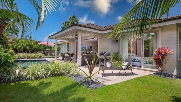 Ein modernes Haus mit überdachter Terrasse, Sitzgelegenheiten im Freien, einem Pool und üppiger Bepflanzung.