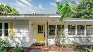 A single-story house with a yellow front door, white siding, and a small front porch. - Banyan Tree Cottage  Tropical Siesta Key Retreat - Walk to Sunset at Shell Beach (Sarasota)