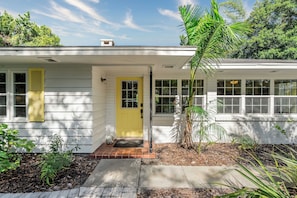 Une maison de plain-pied avec une porte d’entrée jaune, un revêtement extérieur blanc et un petit porche à l’avant.