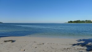 A beach with clear water, a sandy shore, and a distant shoreline with trees and buildings. - Banyan Tree Cottage  Tropical Siesta Key Retreat - Walk to Sunset at Shell Beach (Sarasota)