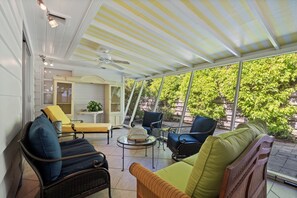 A covered patio with wicker furniture, a glass table, and a ceiling fan. - Banyan Tree Cottage Tropical Siesta Key Retreat - Walk to Sunset at Shell Beach (Sarasota)