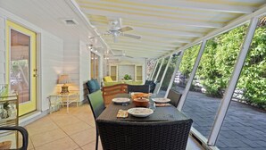 A covered patio with a dining table set for two, surrounded by wicker chairs. - Banyan Tree Cottage  Tropical Siesta Key Retreat - Walk to Sunset at Shell Beach (Sarasota)