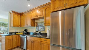 Una cocina con gabinetes de madera, un refrigerador de acero inoxidable y una encimera negra.