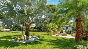 Ein gepflegter Garten mit Palmen, einer Steinkaminfeuerstelle und einer Terrassenanlage mit Gartenmöbeln.
