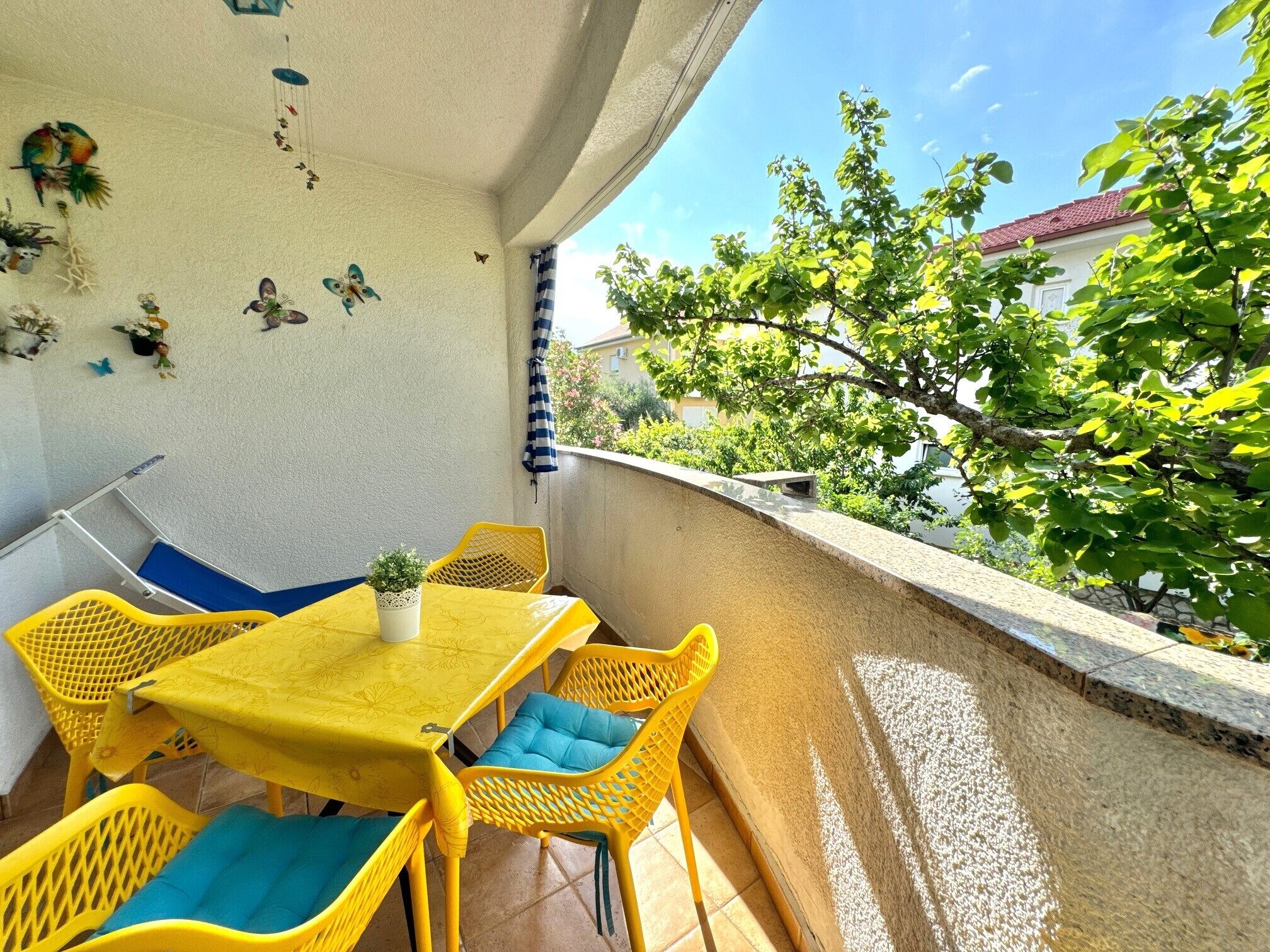 A balcony with a yellow table and chairs, a small potted plant, and decorative wall art.