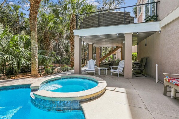 A pool area with a covered seating area, outdoor furniture, and a staircase leading to an upper level.