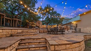 Une terrasse en pierre avec des sièges d’extérieur, une terrasse en bois et des guirlandes lumineuses.