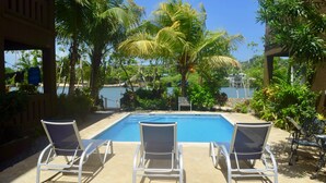 A poolside area with three lounge chairs, a clear blue pool, and lush greenery including palm trees. - Luxury 3 Bedroom/2 Bath Waterfront Condo in a quiet part of West End, Roatán (West End)