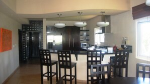 A modern kitchen with dark cabinetry, a central island with bar stools, and pendant lighting. - Luxury 3 Bedroom/2 Bath Waterfront Condo in a quiet part of West End, Roatán (West End)