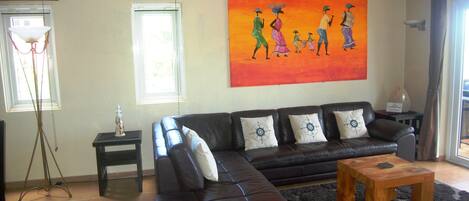 A living room with a sectional sofa, a wooden coffee table, a floor lamp, and a large painting on the wall.