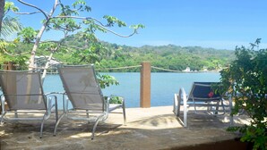 A terrace with two lounge chairs overlooking a body of water, surrounded by greenery and a stone wall. - Luxury 3 Bedroom/2 Bath Waterfront Condo in a quiet part of West End, Roatán (West End)
