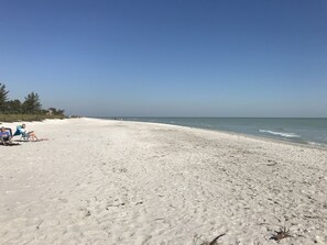 Une plage de sable avec des empreintes et quelques personnes au loin.