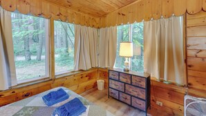 Een houten kamer met een bed, een dressoir en ramen met uitzicht op een bos.