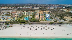 A resort with multiple buildings, a large sandy beach, and a clear blue sea.