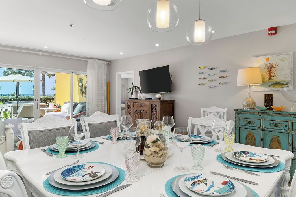 A dining area with a white table set for two, surrounded by white chairs. A television is mounted on the wall, and there are decorative fish on the wall.