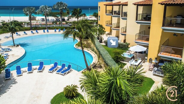 A resort with a large pool, sun loungers, and a view of the beach.