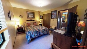 A hotel room with a bed, a desk with a computer, a chair, a lamp, and a television.