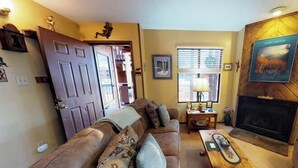 A living room with a sofa, a coffee table, a fireplace, and a door leading to another room.