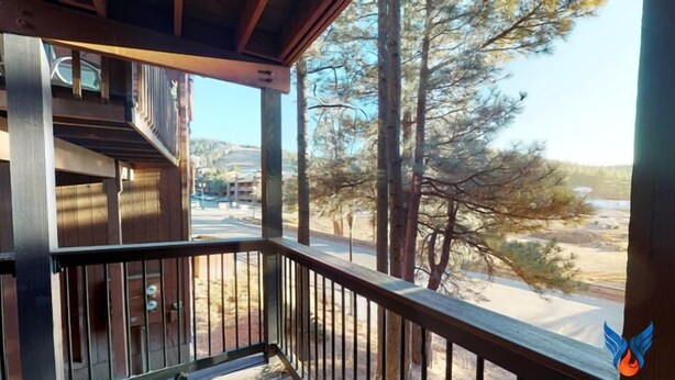A wooden balcony with a metal railing overlooking a road and trees.