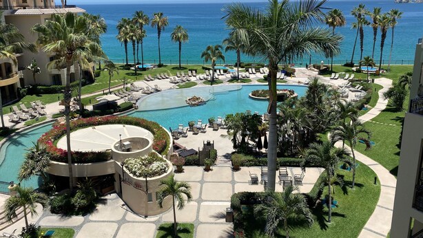 A resort with a large pool, palm trees, and a view of the ocean. - 2BR at Estancia on Medano Beach! (Cabo San Lucas)