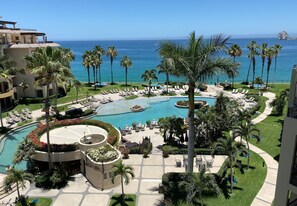 A resort with a large pool, palm trees, and a view of the ocean. - 2BR at Estancia on Medano Beach! (Cabo San Lucas)