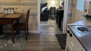 A compact kitchen with a stove, a dining area with a table and chairs, and a cozy living space with a couch and a lamp.
