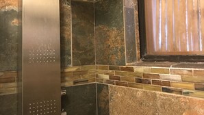 A bathroom with a shower enclosure, stone walls, and a wooden window.