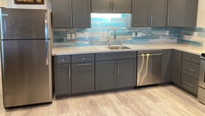 Une cuisine moderne avec des meubles gris, des appareils en acier inoxydable et un pare-feu en carreaux bleus.