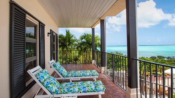 Een overdekt balkon met twee loungestoelen, uitzicht op zee en een tropisch landschap.