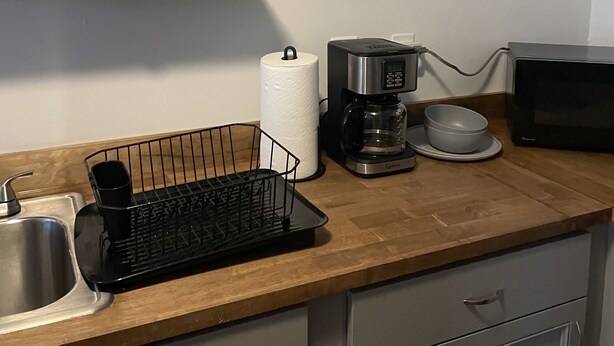 Een keuken met een houten aanrecht, een koffiezetapparaat, een magnetron en een bordje met de tekst 'this home with love & laughter'.